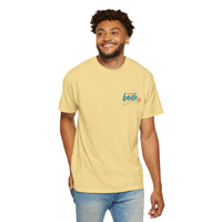 A man wearing the BODE Summer Camp T-Shirt 2026 "Life's Better Together" by Printify stands against a plain background, smiling. The light yellow heavyweight cotton tee features a small colorful graphic and text on the left chest.