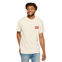 A man stands smiling with one hand in his pocket, wearing a Printify BODE Summer Camp T-Shirt 2026 "Throwback Sunset" (Unisex Comfort Colors 1717), featuring "CAMP BODE" in red on the front.