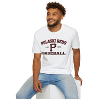 A man in a Printify "P Reds Baseball Est. 1978 - Unisex Softstyle T-Shirt Volume" and jeans sits on a white block, smiling and looking slightly to the side.