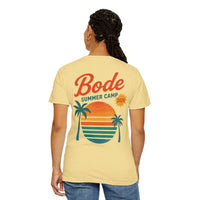 Person wearing the Printify BODE Summer Camp T-Shirt 2026 "Throwback Sunset" (Unisex Comfort Colors 1717) featuring a vintage sunset, palm trees, and stripes graphic on the back.