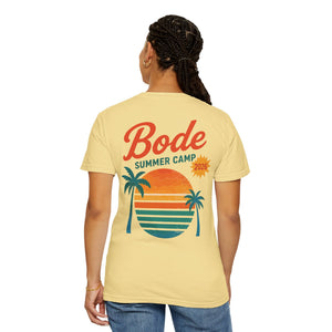 Person wearing the Printify BODE Summer Camp T-Shirt 2026 "Throwback Sunset" (Unisex Comfort Colors 1717) featuring a vintage sunset, palm trees, and stripes graphic on the back.