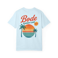 The BODE Summer Camp T-Shirt 2026 "Throwback Sunset" by Printify features "Bode Summer Camp 2026" text and a vibrant palm tree sunset graphic on a light blue Comfort Colors 1717 tee for a vintage-inspired, soft feel. Unisex fit.