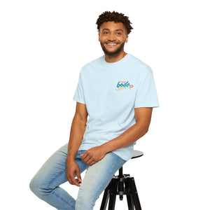 A man in a BODE Summer Camp T-Shirt 2026 "Life's Better Together" by Printify and light jeans sits on a black stool against a white background, smiling at the camera.