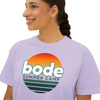 A person wearing the Printify 2026 Bode Summer Bootcamp - Cali Sunset Logo Crop T-Shirt (3023CL), featuring a sunset graphic and "bode SUMMER CAMP" on soft ring-spun cotton.