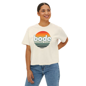 A person in blue jeans smiles while wearing the Printify 2026 Bode Summer Bootcamp - Cali Sunset Logo Crop T-Shirt (3023CL), crafted from 100% ring-spun cotton.