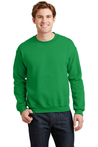 A person wearing a Gildan Heavy Blend Crewneck Sweatshirt 18000 in green and jeans stands smiling against a plain background.