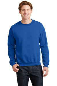 A person wearing a Gildan Heavy Blend Crewneck Sweatshirt 18000 in blue and dark jeans stands against a white background, smiling.