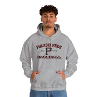 A young man stands with hands in the pocket of a Printify Pulaski Reds Baseball Est. 1978 Unisex Heavy Blend™ Hooded Sweatshirt, featuring "Pulaski Reds Baseball Est. 1978" printed on the front.