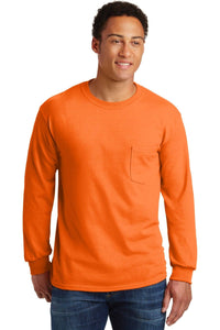 A man wears a bright orange Gildan Ultra Cotton Long Sleeve T-Shirt with chest pocket and custom printed logo, paired with blue jeans, standing facing forward and smiling slightly.