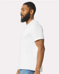A bearded man in profile wears a plain white Gildan 64000 Softstyle® T-shirt (pack of 36, custom screen printed logo included) and blue jeans, standing against a light background.