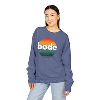 Woman in a blue Printify 2026 Bode Summer Bootcamp Crewneck Sweatshirt (GDH400) with a sunset graphic, standing and looking at the camera with a neutral expression.