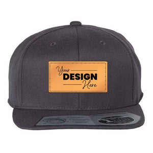 The Flexfit 110® Flat Bill Snapback Hat by Flexfit features a structured six-panel design in gray with a leather patch on the front that reads "Your Design Here" in black letters. The snapback closure guarantees a perfect fit, and its acrylic/wool/spandex blend provides both comfort and durability.