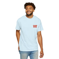 A man smiles against a plain background, wearing the Printify BODE Summer Camp T-Shirt 2026 "Throwback Sunset" in light blue, featuring "CAMP BODE" in red on the left chest. Unisex Comfort Colors 1717.
