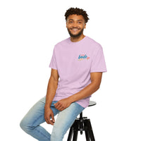 A man smiles on a black stool, wearing the BODE Summer Camp T-Shirt 2026 "Life's Better Together" by Printify—Unisex Comfort Colors 1717 in light purple with light blue jeans, set against a white background.