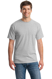 A man stands facing forward, smiling, wearing a Gildan Heavy 100% Cotton Custom T-Shirt (Gildan 5000) in light gray with short sleeves and blue jeans, against a white background.