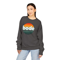 A person in a Printify 2026 Bode Summer Bootcamp Crewneck Sweatshirt GDH400, featuring a “bode SUMMER CAMP” sunset logo, paired with light blue jeans, stands against a plain background.