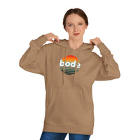 A person wears the Printify 2026 Bode Summer Bootcamp — Cali Sunset Hoodie Sweatshirt (SS4500), a tan cotton-poly fleece hoodie with front pocket, featuring a “bode summer camp” sunset logo.