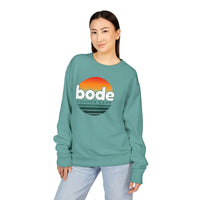 A woman wears the Printify 2026 Bode Summer Bootcamp - Crewneck Sweatshirt GDH400, featuring a teal vintage wash and sunset graphic, against a white background.