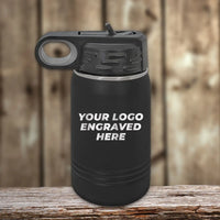 A black water bottle from Kodiak Coolers, featuring a looped lid and custom engraving with "YOUR LOGO ENGRAVED HERE" on its surface, displayed on a wooden surface with a blurred wooden background, makes an excellent promotional gift alongside personalized mugs. Get this Custom Engraved Drinkware with your Logo at no setup fee and only $200 minimal order required during the SPECIAL 72 HOUR SALE PRICING Z.