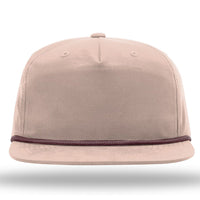 A Richardson 256 Umpqua Rope Snapback Cap, featuring a beige color with brown trim around the visor, is displayed against a white background. This custom rope hat with a leather patch provides UPF 50+ protection.