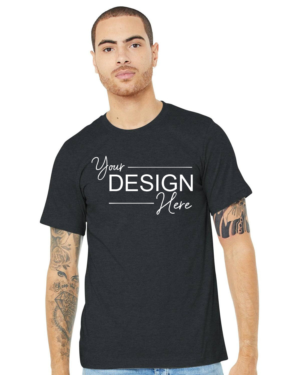 A person sporting a Bella + Canvas Unisex Heather CVC Short Sleeve T-Shirt BC3001CVC in black, featuring "Your Design Here" inscribed on it. The Airlume Cotton fabric enhances the tattooed arms on display.