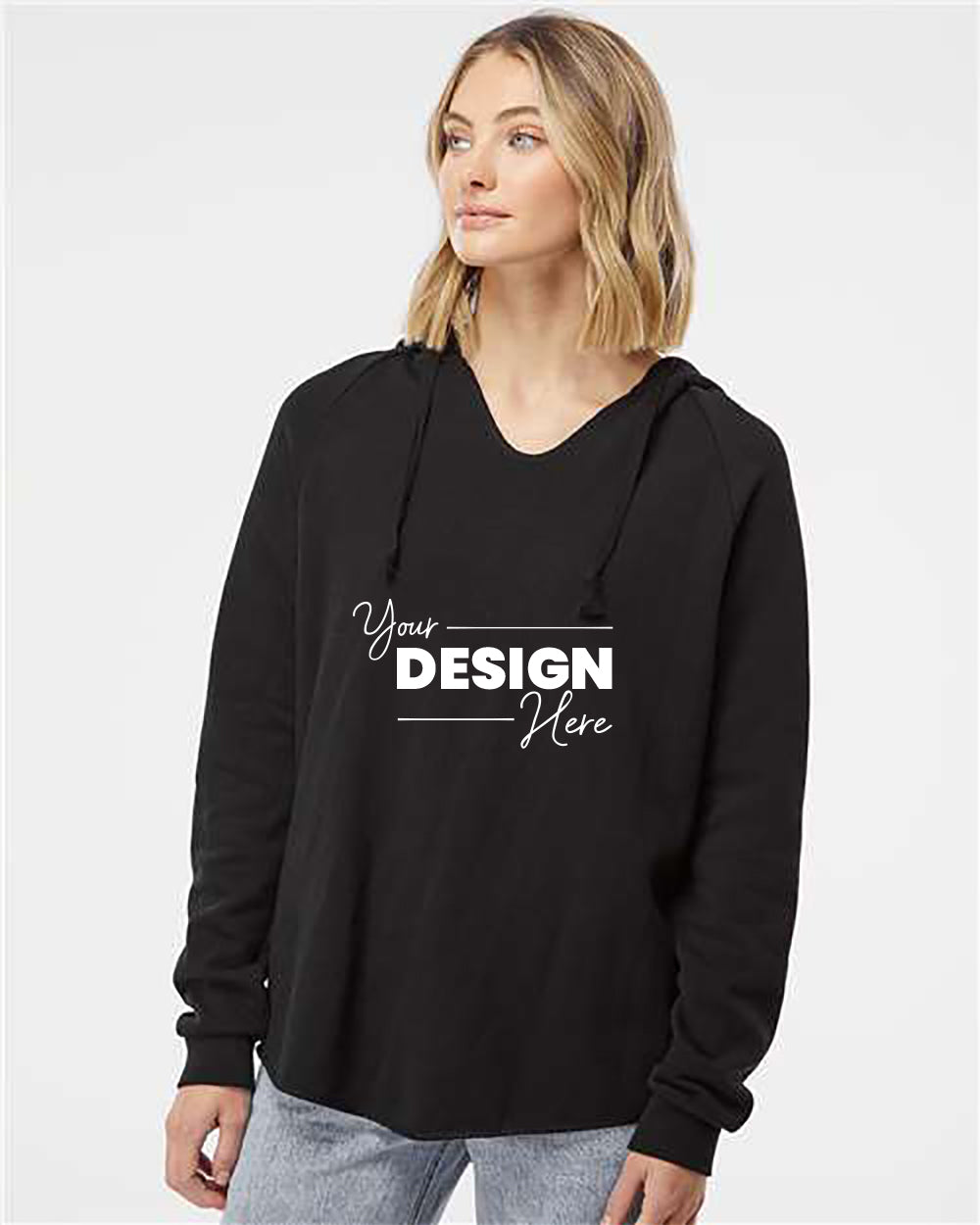 Woman wearing an Independent Trading Co. Women Lightweight California Wave Wash Hoodie Sweatshirt with the text "Your Design Here" printed on the front, paired with light blue jeans, standing against a plain white background.