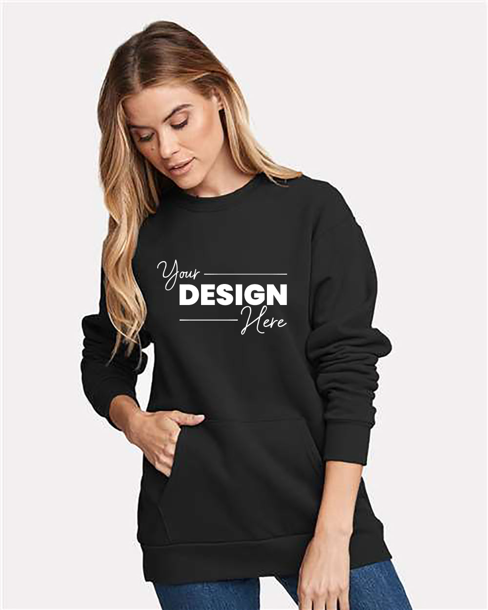 A woman with long hair wearing a black Next Level Unisex Santa Cruz Pocket Crewneck Sweatshirt made of heavyweight fabric with "Your Design Here" printed on the front and blue jeans, standing against a plain white background.