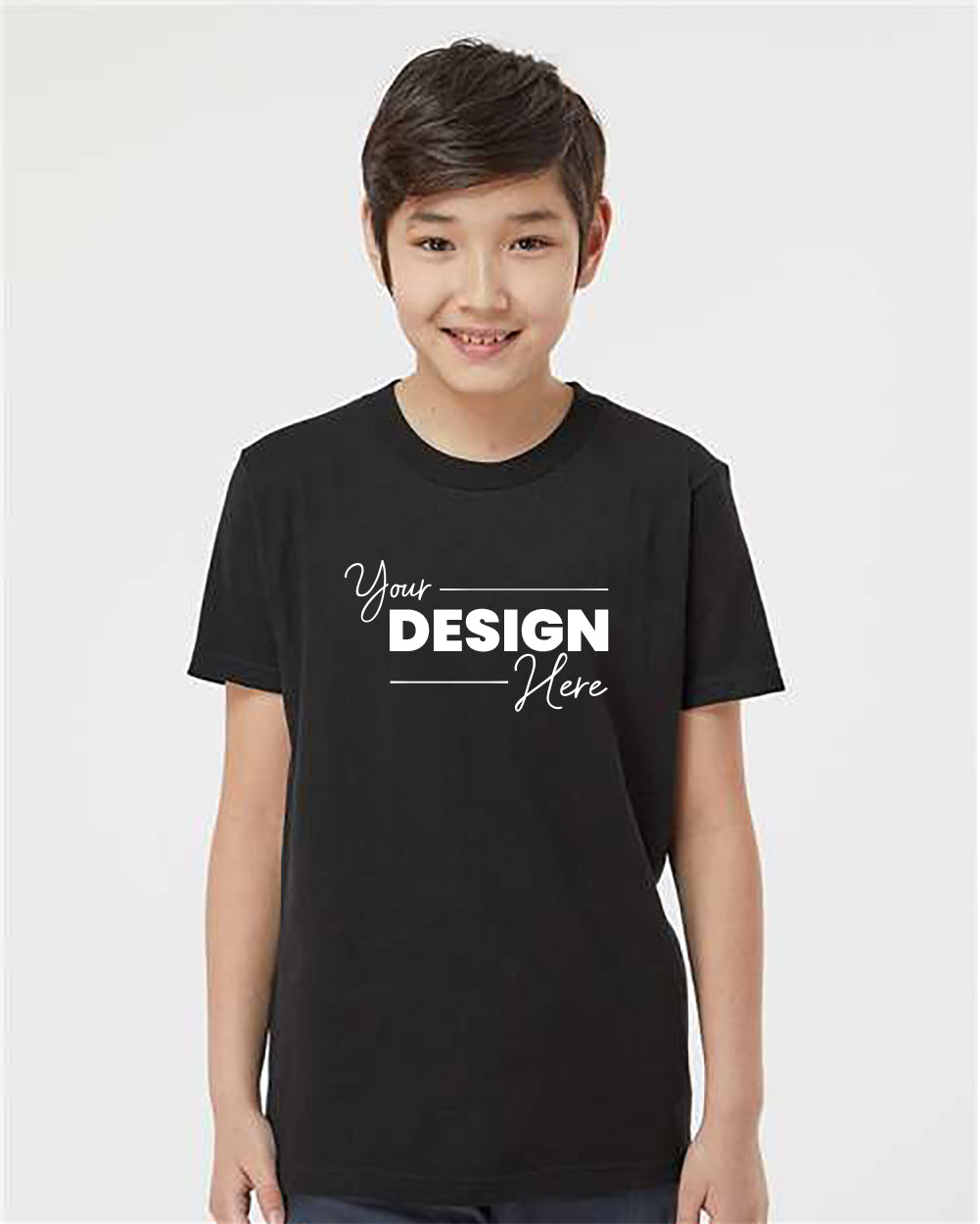 A young person with short hair smiles while wearing a black Tultex Youth Fine Jersey T-Shirt 100% Cotton that has the text "Your Design Here" printed on the front.