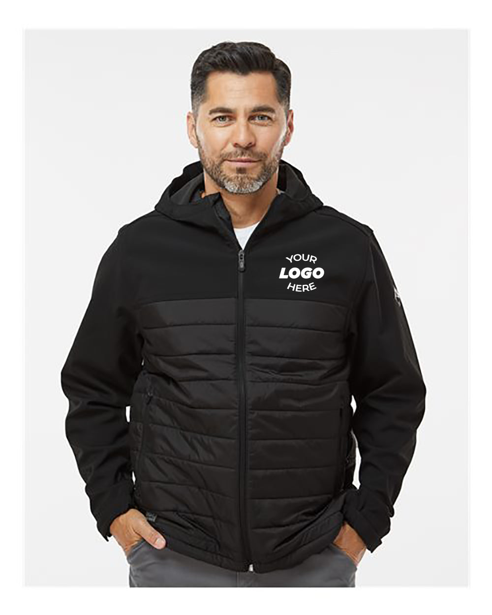 A man stands against a plain background, wearing the DRI DUCK Pinnacle Soft Shell Puffer Jacket. The black jacket, which features insulation and a hood, also includes a logo area on the left chest.