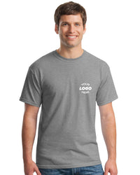 A man in a Gildan Heavy 100% Cotton Custom T-Shirt (Pack of 36), featuring a white "Your Logo Here" screen-printed on the left chest, stands and smiles.