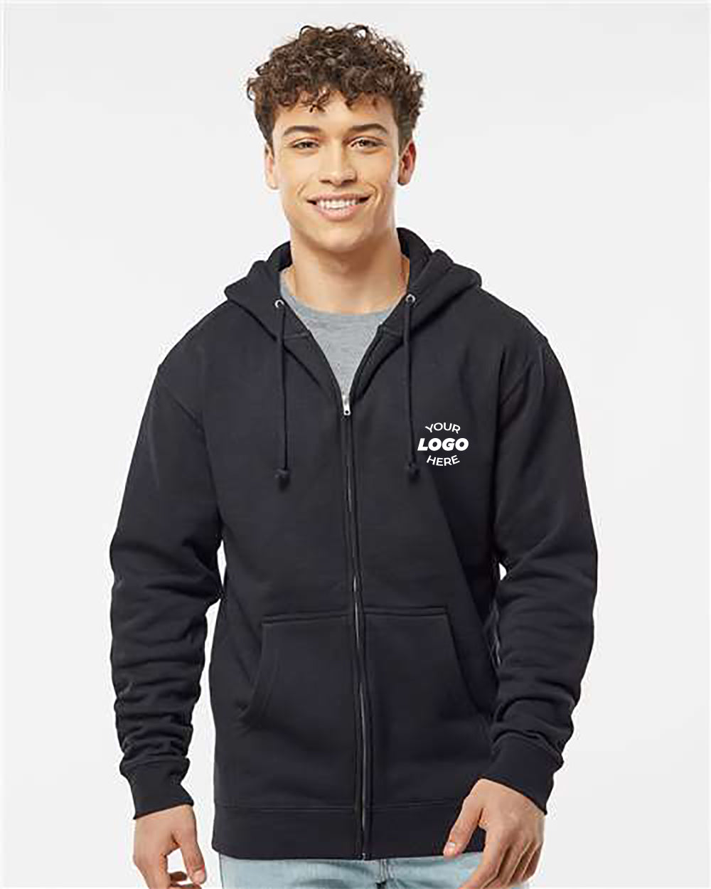 A person wearing an Independent Trading Co. Heavyweight Full-Zip Hoodie Sweatshirt with a "Your Logo Here" placeholder on the chest, over a gray t-shirt and light blue jeans, standing against a plain background.