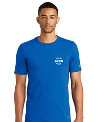 A man wearing a Nike Dri-FIT Cotton/Poly T-Shirt NKBQ5231, featuring "Your Logo Here" printed on the chest in blue and designed for efficient moisture-wicking, is standing against a plain white background.