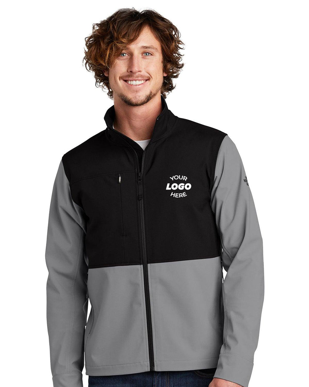 A man smiles against a white background, wearing The North Face Castle Rock Soft Shell Jacket (NF0A552Z) in two-tone black and gray with WindWall fabric and "Your Logo Here" printed on the left chest.