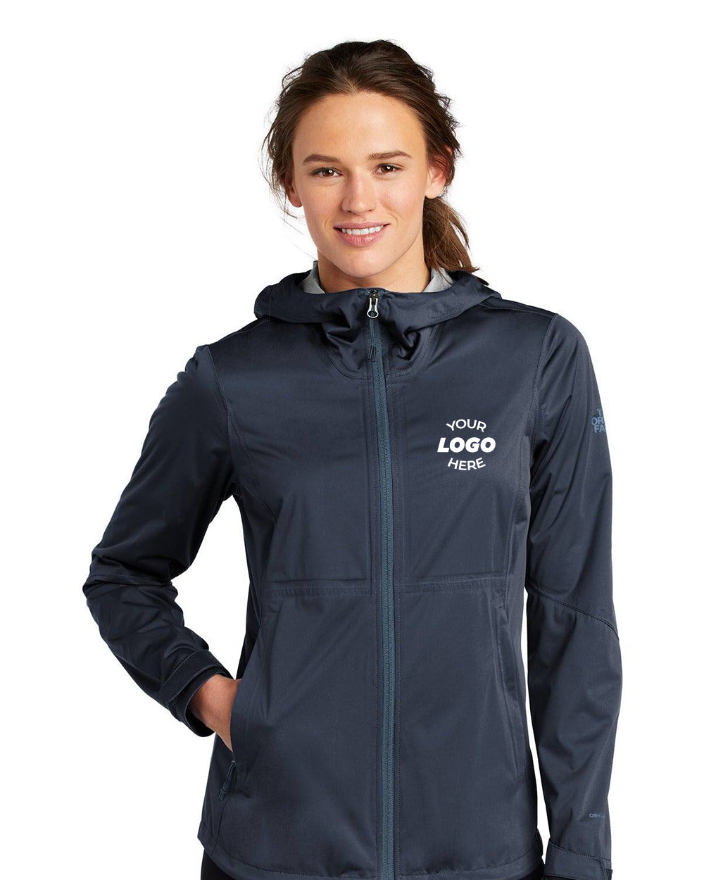 A smiling person wears The North Face Ladies All-Weather DryVent Stretch Jacket NF0A47FH with a customizable front logo. This waterproof jacket boasts an adjustable hood for comfort and style.