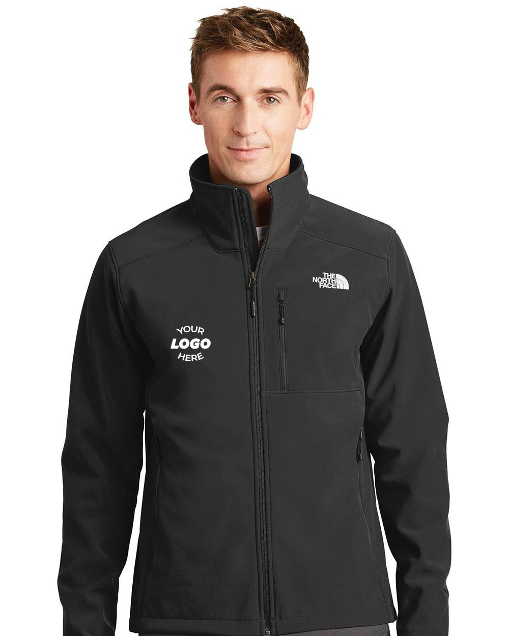A man wears The North Face Apex Barrier Soft Shell Jacket (NF0A3LGT) in black, featuring WindWall fabric, “Your Logo Here” on the left chest, and The North Face logo on the right chest.