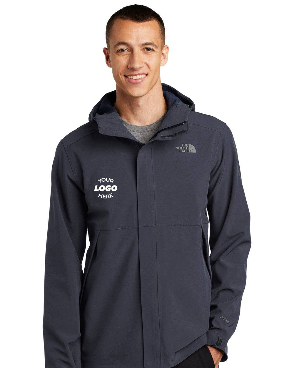 A person wears The North Face Apex DryVent Jacket NF0A47FI in dark gray with “YOUR LOGO HERE” and The North Face branding on the front; its windproof fabric stands out against a plain white background.