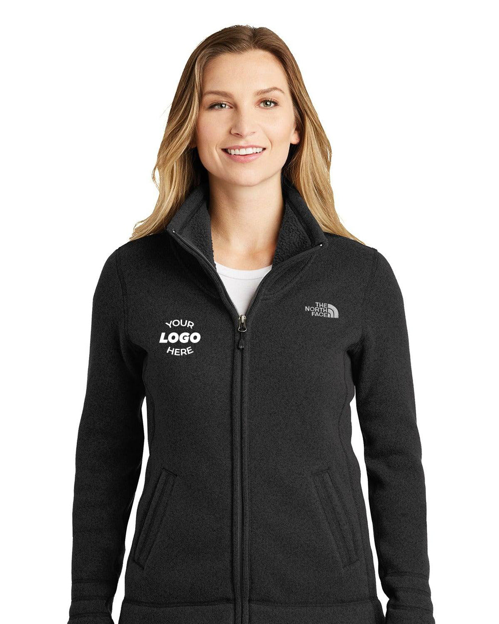 A woman wears The North Face Ladies Sweater Fleece Jacket (NF0A3LH8), displaying the brand's emblem on the right and a mock logo on the left. This black fleece features a brushed fleece interior for enhanced comfort.