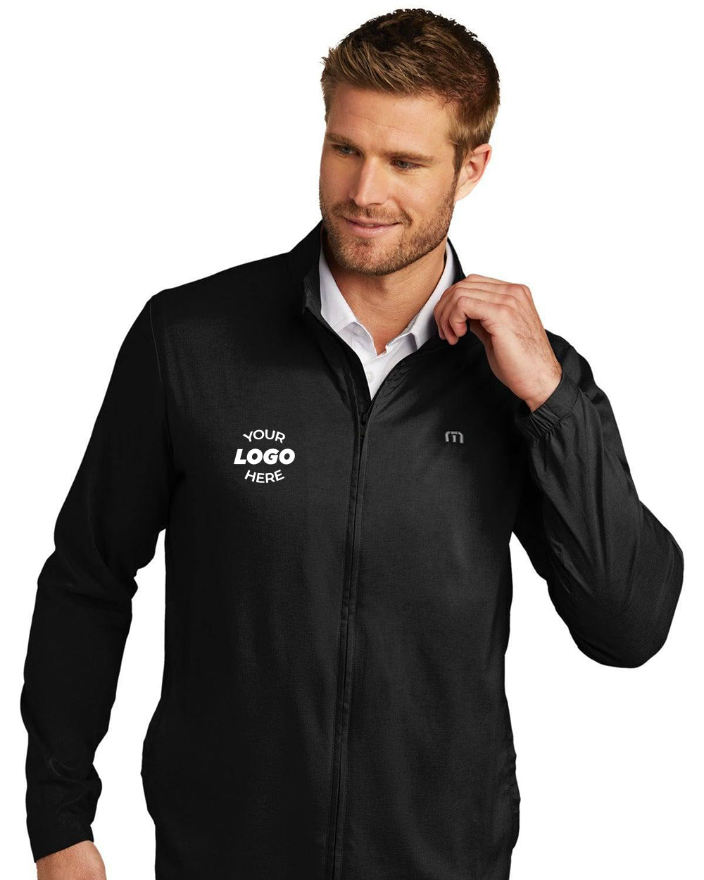 A man wears the TravisMathew Surfside Full-Zip Jacket (TM1MU422) featuring a small "YOUR LOGO HERE" area on the left chest, standing against a white background.
