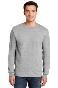 A man wearing a light gray Gildan 100% US Cotton Long Sleeve T-Shirt (Pack of 36, style 2400, custom screen printed logo included) and blue jeans stands facing forward, smiling.