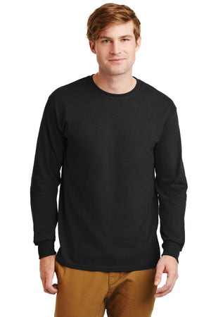 A man faces forward against a white backdrop wearing brown pants and a black Gildan 2400 long sleeve T-shirt, made from 100% US cotton, featuring a custom screen printed logo. This product is sold in packs of 36.