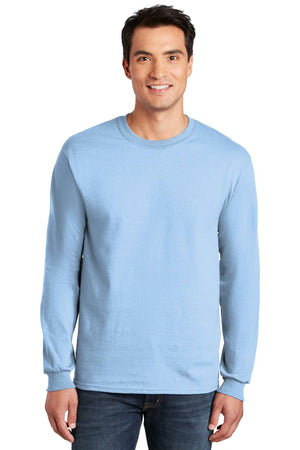 A man in jeans smiles at the camera, wearing a light blue Gildan 100% US Cotton Long Sleeve T-Shirt (Pack of 36, Style 2400) with custom screen printed logo, against a plain white background.