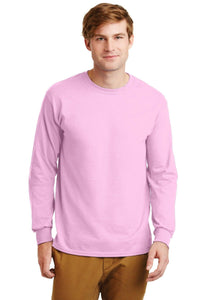 A man in a Gildan 2400 long-sleeve pink T-shirt, made of 100% US cotton with a custom-printed logo, and brown pants stands facing the camera against a plain white background.