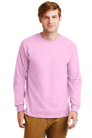 A man in a Gildan 2400 long-sleeve pink T-shirt, made of 100% US cotton with a custom-printed logo, and brown pants stands facing the camera against a plain white background.