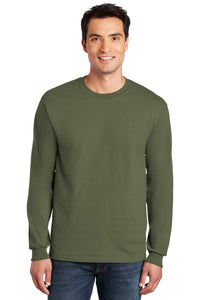 A man smiles facing forward, wearing blue jeans and a plain olive green Gildan 2400 long sleeve T-shirt made from 100% US cotton, with custom screen printed logo included (pack of 36).