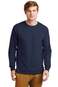 A man with light brown hair is wearing a navy blue Gildan 2400 long-sleeve T-shirt, made from 100% US cotton, with a custom screen printed logo, and tan pants, standing against a plain white background.