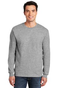 A man wears a Gildan 100% US Cotton Long Sleeve T-Shirt (Pack of 36, custom logo included) and blue jeans, smiling at the camera against a white background.