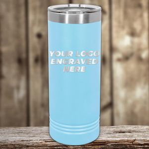 A light blue Custom Logo 22 oz Skinny Tumbler with "your custom logo engraved here" text, displayed on a wooden surface against a blurred background by Kodiak Coolers.