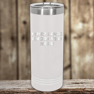 A white insulated Custom Logo 22 oz Skinny Tumbler with "your custom logo here" text, placed on a wooden surface against a blurred background. (Kodiak Coolers)