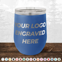 A blue Kodiak Coolers 12 oz stemless wine cup with a metallic lid sits on wood, displaying "YOUR LOGO ENGRAVED HERE." No minimum order—customize with your design. Various color options shown. Perfect for custom engraved mugs.