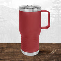 A Kodiak Coolers Wisconsin Luxemburg Casco Spartans 20 oz travel mug with handle and clear lid sits on wood, showing its laser-engraved design against a faint mountain landscape in the background.